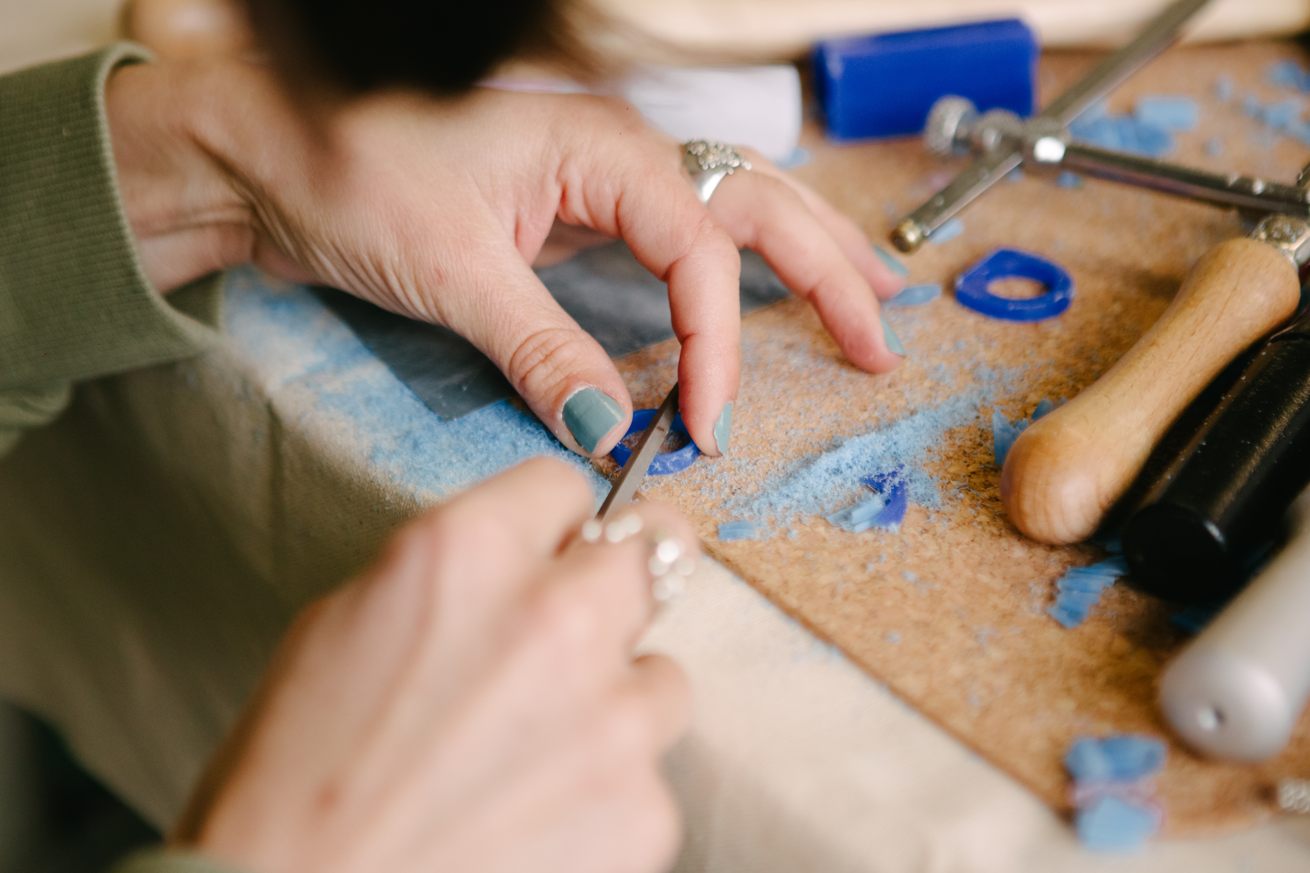 Hands shaping a blue resin glass using a filing tool